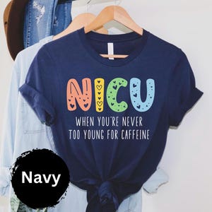 May include: Navy blue t-shirt with a colorful "NICU" graphic and the text "When you're never too young for caffeine".