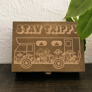 May include: A wooden box with a light brown finish. The box has a design of a van with mushrooms and the text "STAY TRIPPYY" on the front.