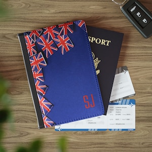 May include: A blue passport holder with a Union Jack pattern and the initials "SJ" in red. The holder is lying on top of a blue passport and two airline boarding passes.