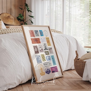 以下が含まれることがあります： さまざまな色のヴィンテージ旅行切手のコレクションを特徴とする額入りのプリント。切手には、ランドマーク、テキスト、イラストの画像が含まれています。フレームは明るい色の木で、プリントは白い寝具のベッドに寄りかかっています。