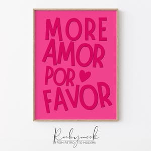 May include: A rectangular wall art print in a light wood frame featuring a vibrant hot pink background with the dark pink text MORE AMOR POR FAVOR and a small heart symbol. The design uses bold, sans-serif lettering centered on the print.