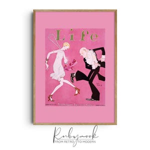May include: A framed print of a vintage "Life" magazine cover. The cover features a pink background with the word "Life" in gold lettering. The illustration depicts a woman and a man dancing. The frame is a light brown color.