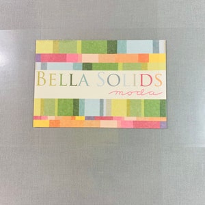 May include: A colorful card with a striped pattern in shades of green, yellow, orange, pink, and blue. The text "BELLA SOLIDS moda" is printed in white on the card.