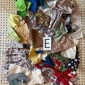 May include: A collection of fabric scraps in various colors and patterns, including floral, polka dot, and animal print. The fabrics are arranged on a patterned surface, with a white letter "E" visible.