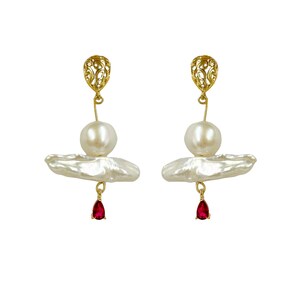 May include: Gold earrings featuring a baroque pearl and a red gemstone drop. The pearl is set within a gold filigree design.