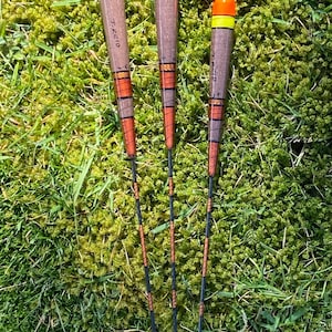 May include: Three wooden fishing bobbers with orange and yellow tops. The bobbers are decorated with black and orange stripes. The bobbers are labeled "J. Reid" and "J. Reid Jr."