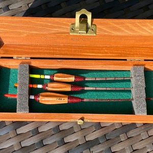 Peut inclure: Une boîte en bois avec un loquet en laiton, contenant trois flotteurs de pêche en bois. Les flotteurs sont rouge, orange et jaune avec des marques noires et blanches. La boîte est doublée de feutre vert et possède un séparateur en mousse.