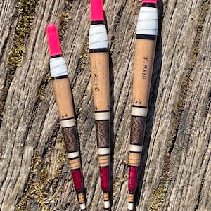Peut inclure: Trois flotteurs de pêche en bois avec des sommets roses et des rayures blanches et brunes. Les flotteurs sont étiquetés "J. Reid" et portent des numéros.
