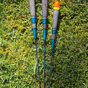 May include: Three fishing bobbers with orange and yellow tops and blue and black stripes. The bobbers are made of wood and have a black line attached to them.