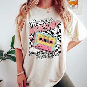 Puede incluir: Una camiseta de color crema con un gr&aacute;fico retro de una cinta de casete con el texto "Made to Worship" y "Psalms 150:6" y la frase "Let everything that has breath praise the Lord".