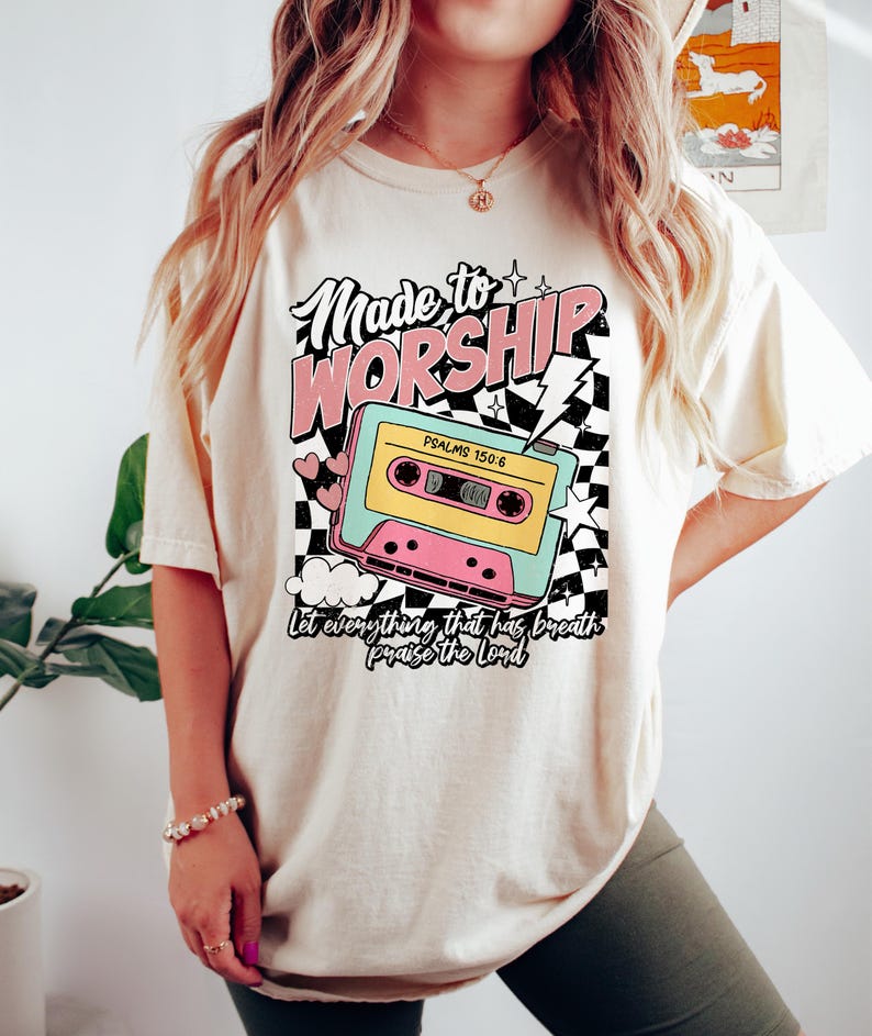 Puede incluir: Una camiseta de color crema con un gr&aacute;fico retro de una cinta de casete con el texto "Made to Worship" y "Psalms 150:6" y la frase "Let everything that has breath praise the Lord".