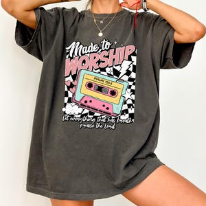 Puede incluir: Una camiseta gris antracita de gran tama&ntilde;o con un estampado gr&aacute;fico de una cinta de casete, un rayo y el texto "Made to Worship" y "Psalms 150:6". El texto "Let everything that has breath praise the Lord" tambi&eacute;n est&aacute; impreso en la camiseta.