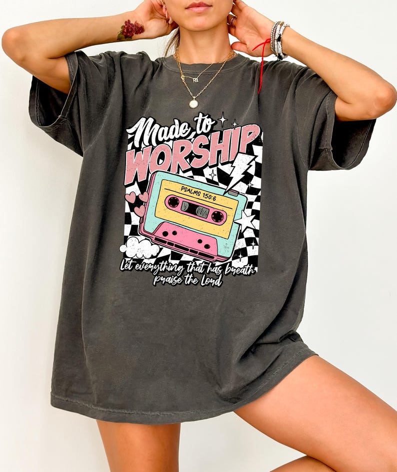 Puede incluir: Una camiseta gris antracita de gran tama&ntilde;o con un estampado gr&aacute;fico de una cinta de casete, un rayo y el texto "Made to Worship" y "Psalms 150:6". El texto "Let everything that has breath praise the Lord" tambi&eacute;n est&aacute; impreso en la camiseta.