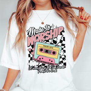 Puede incluir: Camiseta blanca con un gr&aacute;fico de cinta de casete rosa, azul y amarilla. El texto "Made to Worship" est&aacute; por encima de la cinta y "Psalms 150:6" est&aacute; en la cinta. El texto "Let everything that has breath praise the Lord" est&aacute; debajo de la cinta.