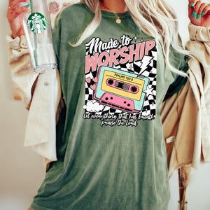 Puede incluir: Camiseta verde con un gr&aacute;fico de casete retro y el texto "Made to Worship" y "Psalms 150:6". El texto "Let everything that has breath praise the Lord" est&aacute; debajo de la cinta de casete.