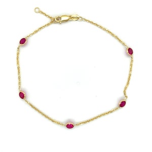 May include: A gold chain bracelet with five oval-shaped ruby red gemstones.