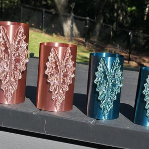 May include: Four cylindrical containers arranged in a row, featuring a raised, textured leaf design on the front. The two larger containers are metallic copper, while the two smaller containers are a deep metallic teal blue.