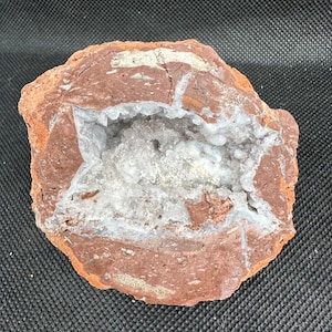 May include: A geode with a reddish-brown exterior and a white, crystalline interior. The geode is partially open, revealing the crystals inside.