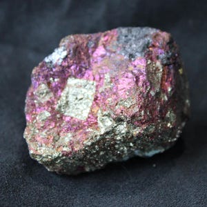 May include: A rough, irregularly shaped rock with a metallic, iridescent surface. The rock is a mix of silver, pink, and black colours.