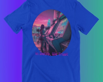 May include: A blue t-shirt with a circular graphic of a person standing in front of a retro arcade game. The graphic has a pink and purple color scheme. The text "In Retro, We Trust" is printed below the graphic.