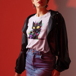 May include: A woman wearing a white t-shirt with a black cat graphic featuring colorful paint splatters. The cat has yellow eyes and a psychedelic design. She is also wearing a black leather jacket, a denim skirt, and red sunglasses.