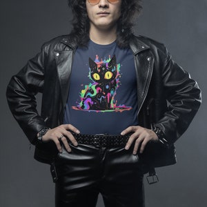 May include: A man wearing a black leather jacket and black leather pants with a navy blue t-shirt featuring a black cat graphic with colorful paint splatters.