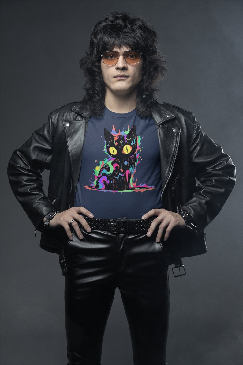 May include: A man wearing a black leather jacket and black leather pants with a navy blue t-shirt featuring a black cat graphic with colorful paint splatters.