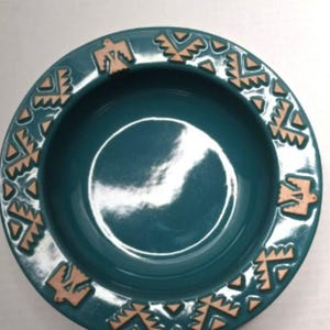 Puede incluir: Un cuenco de cerámica de color turquesa con un borde decorativo que presenta un patrón repetitivo de pájaros estilizados marrones y diseños geométricos.