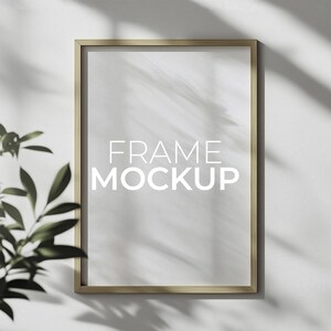 Puede incluir: Una maqueta de marco de color dorado con fondo blanco. El marco está en una pared blanca con una sombra proyectada por el marco. El texto "FRAME MOCKUP" está en el centro del marco.