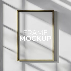 Può includere: Un mockup di cornice in legno semplice su una parete bianca con la luce che splende attraverso una finestra. Il testo "FRAME MOCKUP" è scritto in bianco sulla cornice.