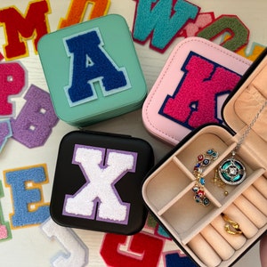 Pode incluir: Uma caixa de joias preta com um interior de feltro branco e vários compartimentos. A caixa é decorada com uma letra X de feltro branco. A caixa é cercada por letras de feltro coloridas.