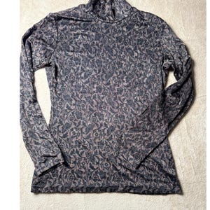 May include: A long-sleeve turtleneck shirt featuring a dark gray and light brown floral pattern. The garment has a fitted silhouette with a high neck and full-length sleeves, showcasing an intricate botanical print across the entire fabric.