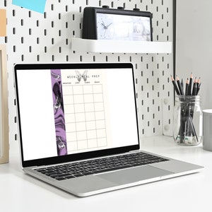 Könnte beinhalten: Ein Laptop-Computer mit weißem Hintergrund, auf dem ein wöchentlicher Meal-Prep-Planer angezeigt wird. Der Planer hat ein lila-schwarzes Marmormuster auf der linken Seite und Spalten für Frühstück, Mittagessen, Abendessen und Snacks.