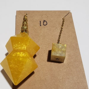 May include: A gold-coloured, double-pointed, crystal pendulum with a gold chain and a small, gold-coloured cube. The pendulum is on a brown card with the number "10" written on it.