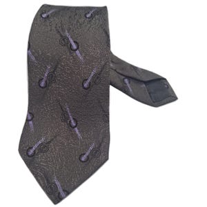 Könnte beinhalten: Eine graue gemusterte Krawatte mit einem violetten Design. Die Krawatte hat eine strukturierte Oberfläche und eine spitze Spitze.