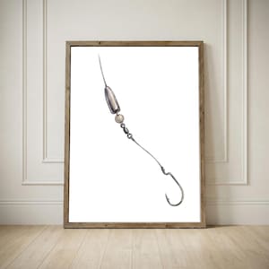 May include: A framed print depicting a fishing hook and tackle illustration. The artwork shows a silver-coloured hook, a weight, and connecting hardware, set against a white backdrop. The frame is a natural wood colour.