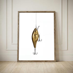 Könnte beinhalten: Gerahmter Druck eines goldenen Angelköders, der an einem dünnen Draht vor einem weißen Hintergrund hängt. Der Köder hat ein detailliertes Design mit mehreren Haken und wird in einem Holzrahmen präsentiert.