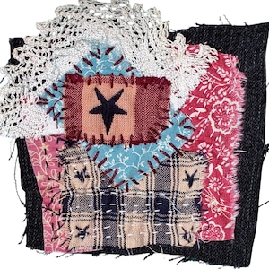 May include: A patchwork textile with a black denim base. It features various fabric scraps in shades of red, pink, blue, and beige, stitched together. A central square has a black star on a peach background. White lace trim adorns the top.