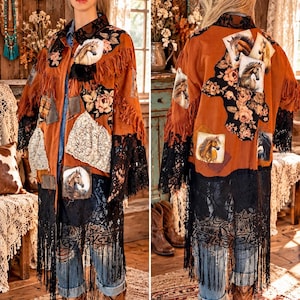 May include: A long, rust-colored jacket featuring a patchwork design with horse portraits, floral patterns, and lace accents. The garment includes fringe detailing along the shoulders and hem, a collared neckline, and long sleeves with black lace trim.