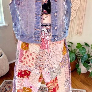 May include: A light blue denim vest with rhinestone buttons and a colourful crochet patch. The vest is paired with a black floral top and patchwork trousers in various floral patterns. The trousers have a drawstring waist and a lace detail.