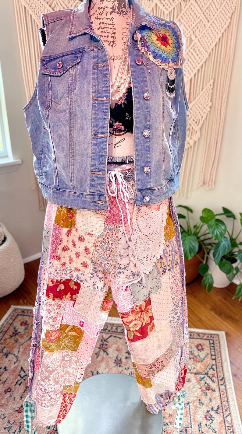 May include: A light blue denim vest with rhinestone buttons and a colourful crochet patch. The vest is paired with a black floral top and patchwork trousers in various floral patterns. The trousers have a drawstring waist and a lace detail.