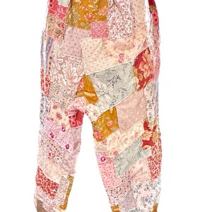 May include: Patchwork trousers in a variety of floral and patterned fabrics. The trousers feature a mix of pinks, reds, yellows, and greens, with an elasticated waistband and gathered ankles. The design is a mix of vintage and bohemian styles.