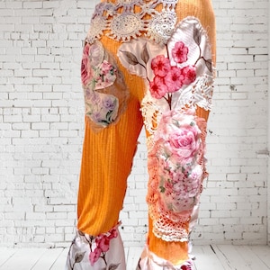 May include: Orange pants with floral and lace embellishments. The pants have a wide leg and a ruffled hem.