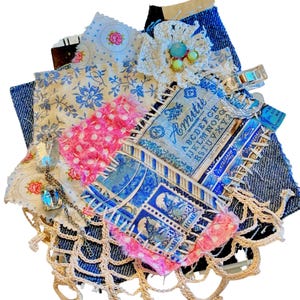 May include: A handmade fabric collage featuring denim, floral, and patterned fabrics. The collage includes a crocheted flower with turquoise and yellow accents, a pink polka dot fabric, and a vintage postage stamp design. A delicate chain with a crystal pendant and a lace trim complete the design.