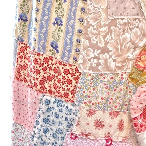 May include: A patchwork textile with a mix of floral patterns in red, blue, pink, and cream. The design includes stripes, small flowers, and larger floral motifs, creating a vintage, handcrafted aesthetic. The fabric pieces are sewn together.