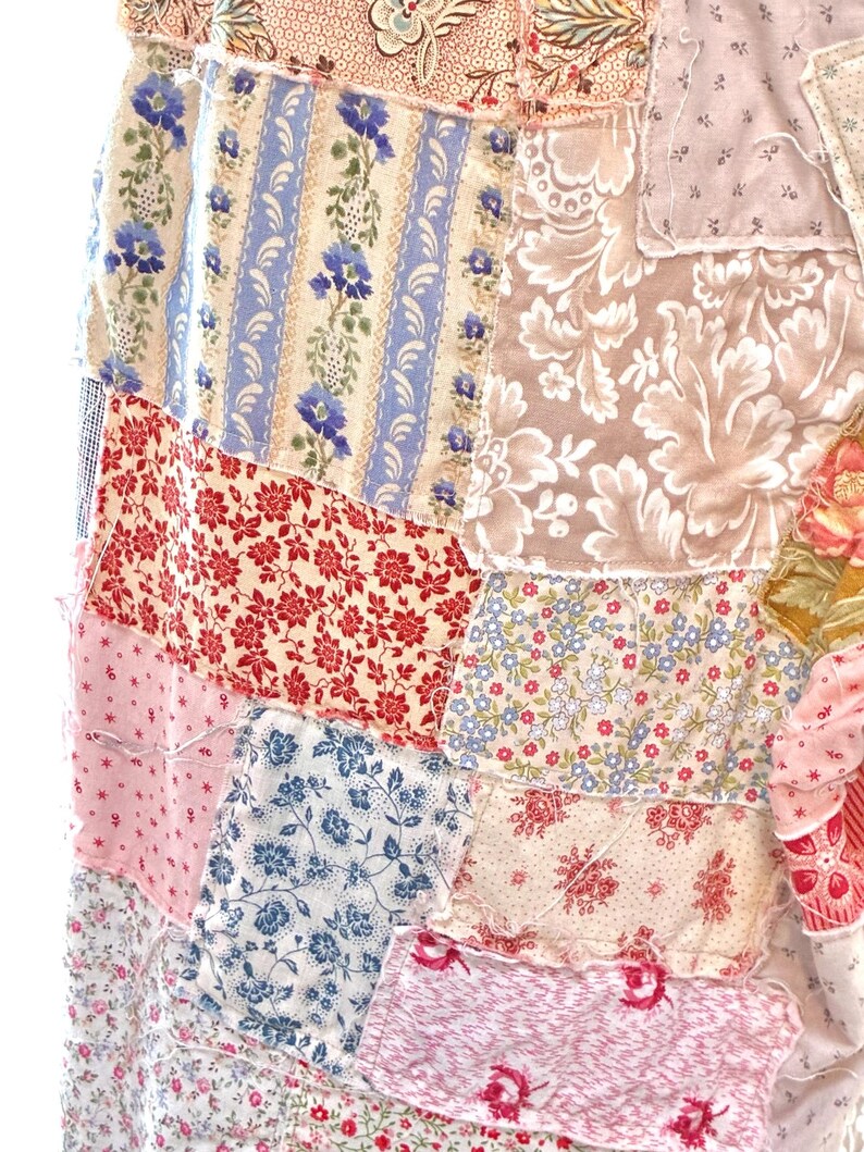 May include: A patchwork textile with a mix of floral patterns in red, blue, pink, and cream. The design includes stripes, small flowers, and larger floral motifs, creating a vintage, handcrafted aesthetic. The fabric pieces are sewn together.