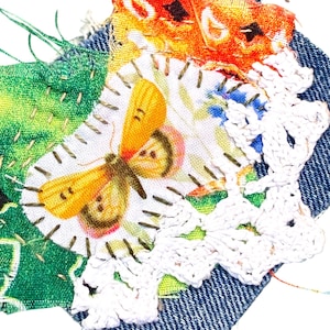May include: A fabric art piece featuring a butterfly design. The artwork incorporates denim, floral, and crochet elements. The butterfly is yellow and orange, with a white background. The piece is stitched together with various colored threads.