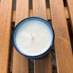 May include: A white candle with a single wick in a blue glass jar with a textured design.