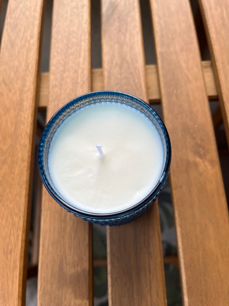 May include: A white candle with a single wick in a blue glass jar with a textured design.