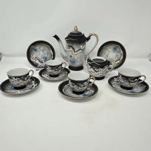 May include: A tea set featuring a teapot, a sugar bowl, and four cups with matching saucers. Each piece is crafted from black and white porcelain with a gradient finish, decorated with a detailed white dragon motif and gold-tone trim accents.